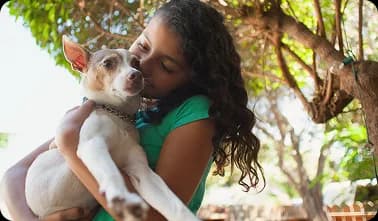 A girl holding a small white puppy in her arms.