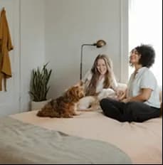 Two people relaxing on a bed with a small dog