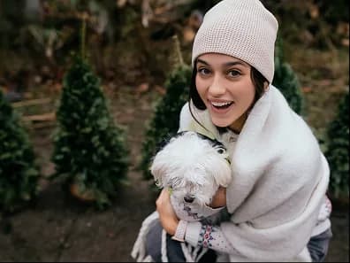 A woman in a knit hat holding a small white dog