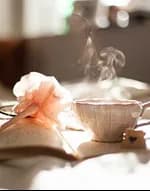 A steaming cup of tea beside pink flowers