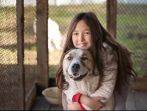 A girl hugging a dog beside a fence.