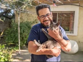 A volunteer holding a cat outdoors.
