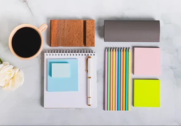 A notebook, coloured pencils, sticky notes and coffee on a marble desk