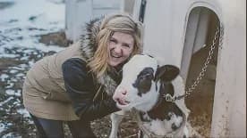 A smiling volunteer cuddling a calf