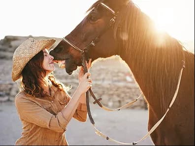 A woman in a sun hat nuzzling a horse