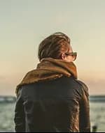 A person in a scarf looking out at the sea