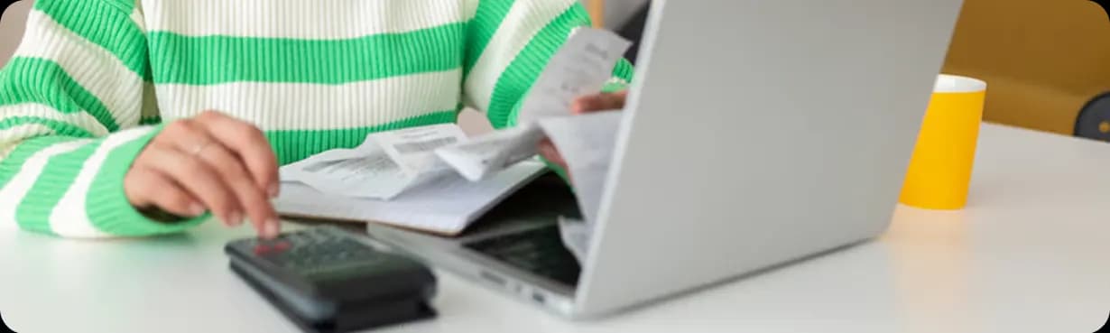 A person using a calculator next to receipts and a laptop