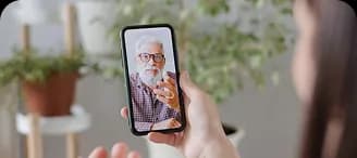 A hand holding a phone showing a video call with an older man