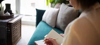 A person writing in a notebook on a sofa