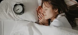 A woman asleep in bed beside an alarm clock